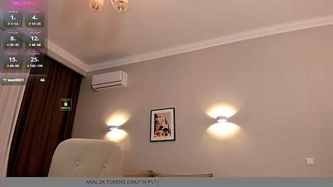 Media: Video of a modern, minimalist bedroom with beige walls, a light beige chair, two wall-mounted lamps, a framed picture, and a ceiling-mounted air conditioner.