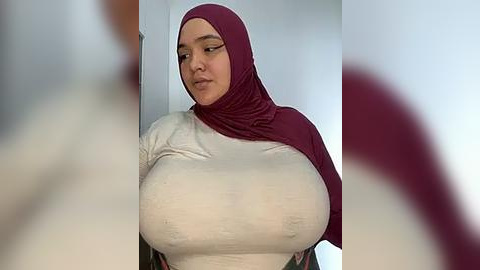 Media: Video of a woman with a medium complexion, wearing a tight, white, long-sleeved shirt and a maroon hijab. Her large, round breasts are prominently displayed. Background is blurred, suggesting a close-up focus.