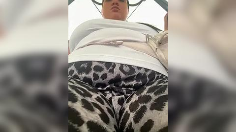 Media: Video of a woman from a low angle, wearing a white top and tight leopard print leggings, showcasing her curvy figure. Her face is partially visible, with a neutral expression. The background is blurred, focusing on her attire.