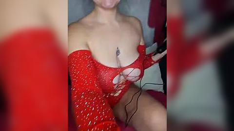 Media: Video of a fair-skinned woman with medium-sized breasts, wearing a red sequined off-shoulder dress, holding a black controller, in a dimly lit room with blurred red background.