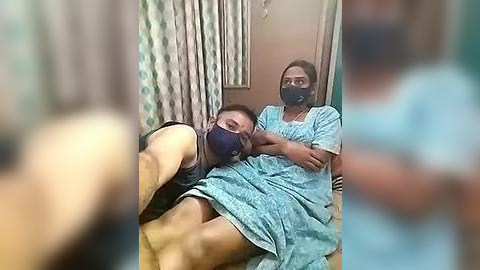 Media: A video shows a young man lying on a bed, wearing a blue mask and hospital gown, with a woman in a similar outfit tending to him, both in a hospital room.