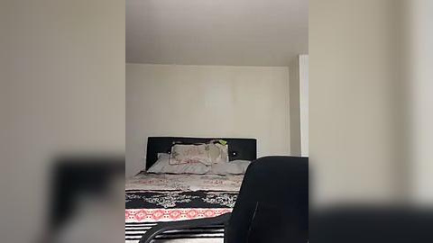 Media: A video of a sparsely decorated, rectangular room with beige walls. A bed with a black headboard and patterned bedspread occupies the center, flanked by two black chairs. The room appears dimly lit.