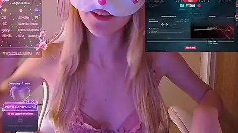 Media: Video of a blonde woman with a white mask, wearing a lace bra, in a dimly lit room, with a Twitch streamer overlay and chat box.