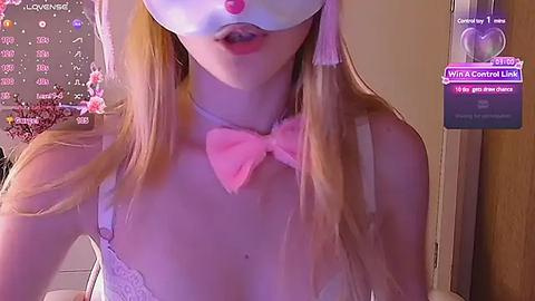 Media: Video of a fair-skinned, blonde woman wearing a white mask, pink bow, and lace bra, with a digital screen showing \"Twitch Central Link\" in the background.