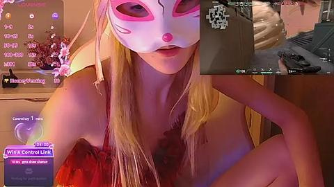 Media: Video of a blonde woman in a pink mask, revealing cleavage, with a blurred background of a bedroom, alongside a Twitch chat screen and a video feed of a man.