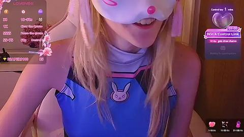 Media: Video of a blonde woman wearing a bunny mask, blue bodysuit with a bunny emblem, and a white high collar, set in a dimly lit room with chat bubbles.