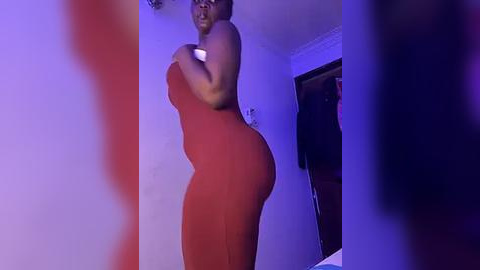 Media: Video of a plus-size Black woman in a red, form-fitting dress, standing in a dimly lit room with purple and red lighting.