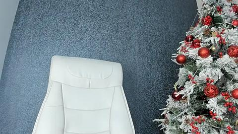 Media: A video shows a cream leather chair against a textured, dark blue wall, with a decorated Christmas tree on the right, adorned with red and gold ornaments and snowflakes.