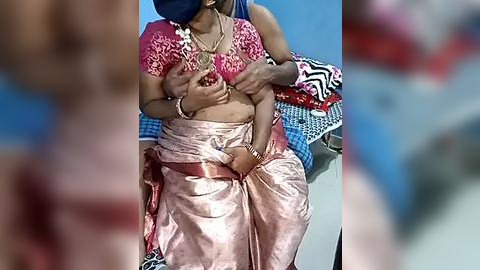 Media: Video of an Indian woman breastfeeding a baby, wearing a pink saree and blue blouse, with colorful fabric in the background.