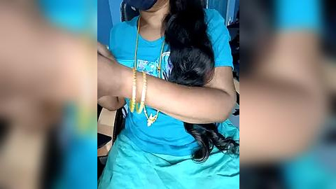 Media: Video of a person with long black hair, wearing a blue shirt and blue skirt, holding a black cat in their arms. Background is blurred, focusing on the person and cat.