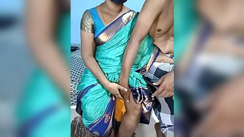 Media: Video: A woman in a teal sari with gold embroidery, seated on a boat, being assisted by a shirtless man with a dark complexion.