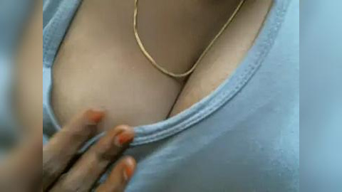 Media: Video of a woman's cleavage in a light blue shirt, with a thin gold necklace and a hand with orange nails gently touching the fabric.