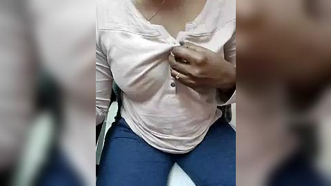 Media: Video of a woman in a white blouse and blue pants, her hand over her chest, blurred background.