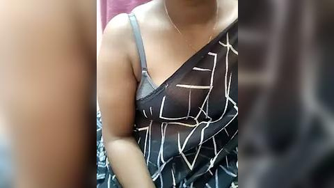 Media: Video of a woman with medium brown skin, wearing a black and white geometric-patterned dress, revealing a gray bra underneath. The background is blurred, with a reddish-brown hue.