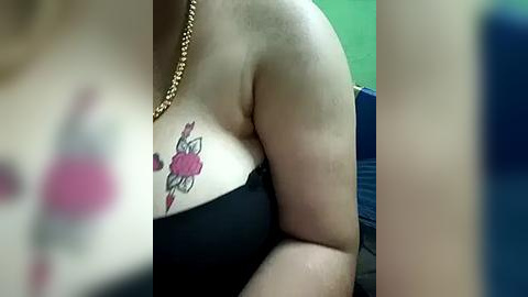 Media: Video of a woman with light skin, wearing a black strapless top, showcasing a colorful tattoo of a pink rose and white leaves on her left breast.