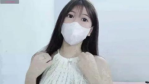 Media: Video of an Asian woman with long black hair, wearing a white face mask, white knit top, and holding her hair. Background is plain white.