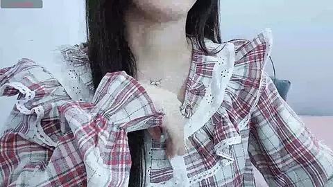 Media: Video of a woman with a bruised face, wearing a plaid shirt, standing indoors. Her face is blurred, and she has a necklace.