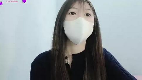 Media: Video of an Asian woman with long black hair and fair skin wearing a white face mask, black sweater, and plain white background.