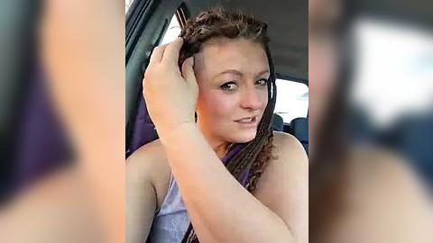 Media: A candid video captures a young woman with fair skin and long, braided hair, adjusting her hair inside a car. She wears a sleeveless top. The background features the car's interior.