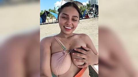 Media: Video of a smiling, light-skinned woman with brown hair in a ponytail, wearing a pink bikini top that exposes her large breasts. She holds a coconut with one hand. Background shows beach umbrellas, palm trees, and a clear blue sky.