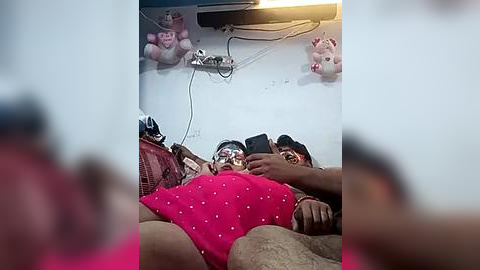 Media: Video of a crowded, dimly-lit train compartment with a man in a pink shirt and woman in a black top, holding a phone, surrounded by stuffed toys and a wire.