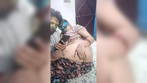Media: A video shows an overweight woman breastfeeding, wearing a striped top and floral skirt, sitting on a patterned bed. A man with a black mask is present, holding her phone.