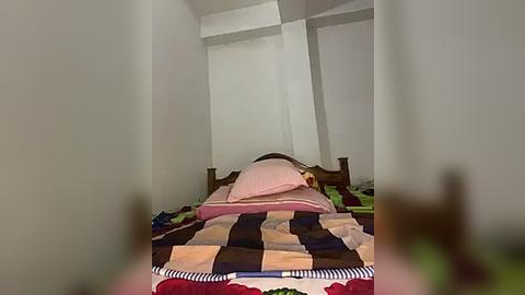 Media: A video of a child's bedroom with a wooden bed and a colorful patchwork quilt, featuring a stuffed animal, and a pink pillow, set against white walls. The room is dimly lit.