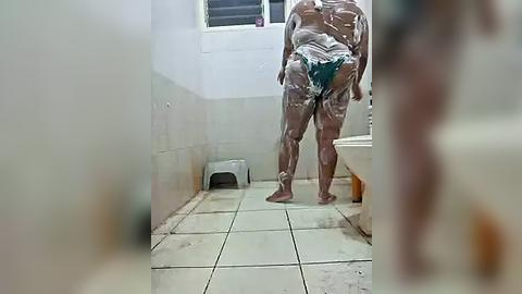 Media: A blurry video of a naked person covered in white powder, standing in a tiled bathroom with a white sink and a metal stool. The person's genitals are visible.