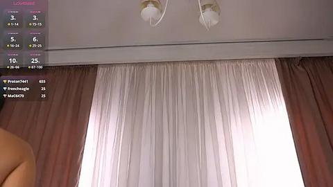 Media: Video of a bedroom with beige curtains partially drawn, revealing a white sheer curtain beneath. Two chandeliers hang from the ceiling, and a digital screen displays a virtual camera feed and viewer statistics.