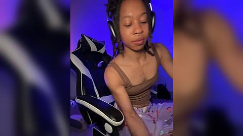 Media: Video of a young Black woman with braided hair, wearing headphones, sitting in a black gaming chair, with a purple-lit room background.