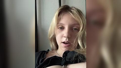 Media: A video of a young, light-skinned woman with shoulder-length blonde hair, wearing a black shirt, speaking into a phone, partially obscured by another person's blurred head.