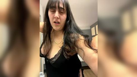 Media: A blurry video of a young woman with long black hair and fair skin, wearing a black lace-trimmed lingerie top, appearing surprised or shocked. Background shows a blurred, indoor setting.