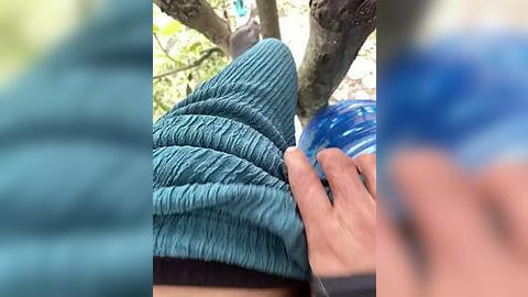 Media: Video of a person wearing a blue, textured knit sweater and a blue helmet, with a blurred background of green leaves and tree trunks.