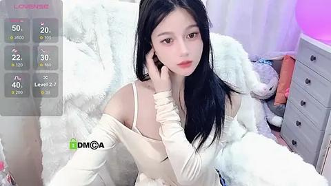 Media: Video of a young Asian woman with long black hair, fair skin, and a slender physique, wearing a white off-shoulder top, sitting on a plush white bed.