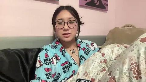 Media: A video of a young Asian woman with dark hair, glasses, and a Hello Kitty pajama shirt, resting on a bed with a cat-patterned blanket.