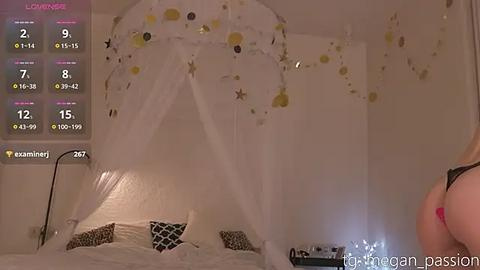 Media: Video of a woman in a black bra standing beside a white canopy bed with gold stars and a white curtain, against a soft pink background.