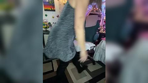 Media: A video captures a woman in a gray, textured dress dancing energetically in a cluttered, colorful room with vibrant posters, a desk, and a chair.