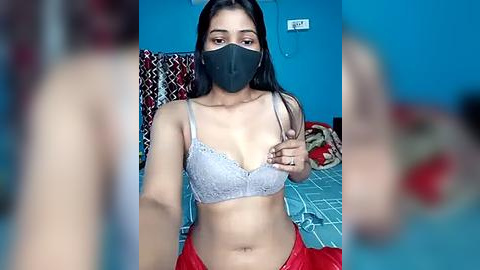 Media: A video of a young South Asian woman with long black hair, wearing a light grey lace bra and red pants, sitting on a bed with a patterned blanket.