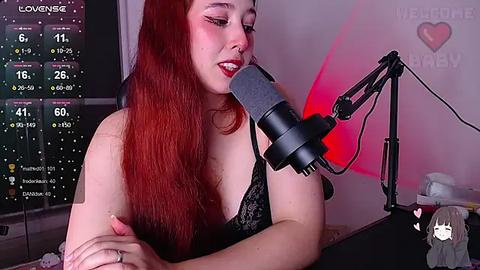 Media: Video of a red-haired woman with fair skin, wearing a black lace bra, singing into a microphone, with a computer screen displaying streaming stats in the background.