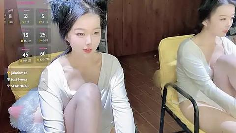 Media: Video of an East Asian woman with fair skin, dark hair styled in twin buns, wearing a white top, sitting on a yellow chair, in a wooden room with a calendar overlay.