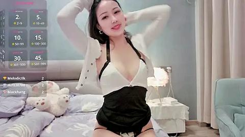 Media: Video of an Asian woman with fair skin, dark hair, and a slim physique, wearing a revealing white and black top, posing seductively on a bed with plush toys in a modern, softly lit bedroom.