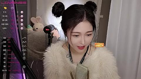 Media: Video of an East Asian woman with fair skin, styled in a chic, dark-haired updo. She wears a fur-trimmed coat and a silver clutch. Background features a plush bunny and a dimly lit room with a \"LOVESICK\" watermark.