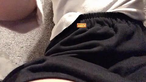 Media: Video of a person's hand and arm, wearing black Nike shorts with an orange logo and white shirt, resting on a grey textured surface.