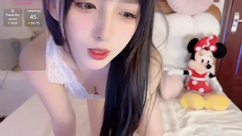 Media: Video of an East Asian woman with long black hair, wearing a white lace bra, lying on a bed with Minnie Mouse plush toy.