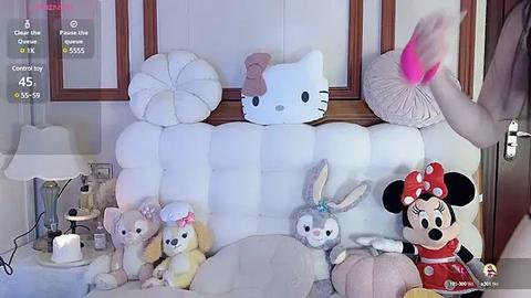 Media: Video of a plush toy collection featuring Hello Kitty, Mickey Mouse, Minnie Mouse, and other characters on a white tufted headboard, with a hand holding a feather pillow.