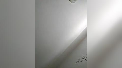 Media: A video of a minimalist interior, featuring a stark white wall with a subtle shadow cast from a ceiling fixture, and handwritten text in Arabic script at the bottom.