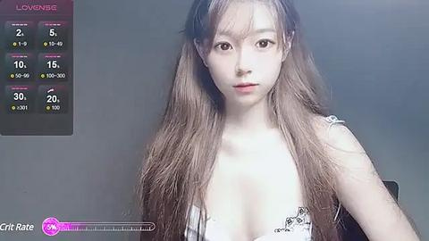 Media: Video of an Asian woman with long brown hair and fair skin, wearing a revealing white lace bra, against a gray background.