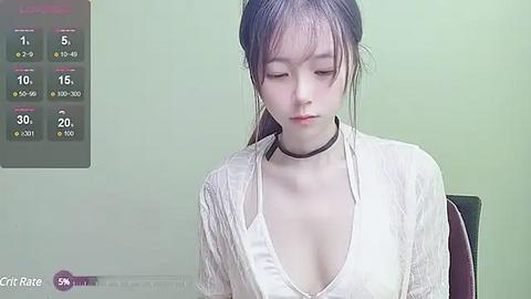 Media: Video of a young Asian woman with pale skin, long dark hair, wearing a low-cut, white, textured blouse, sitting indoors, background showing a weather app with temperatures.