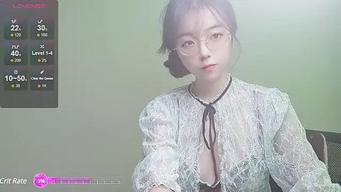 Media: A video of an East Asian woman with fair skin, wearing glasses, a sheer lace top, and a black choker, standing indoors.