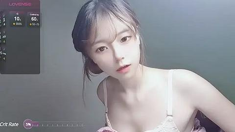 Media: A video of an East Asian woman with fair skin, long brown hair, and a slender physique, wearing a white lace bra, in a dimly lit room.